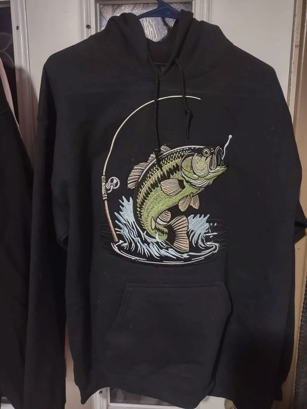 Black hoodie embroidered with a largemouth bass leaping out of the water at a fishing line