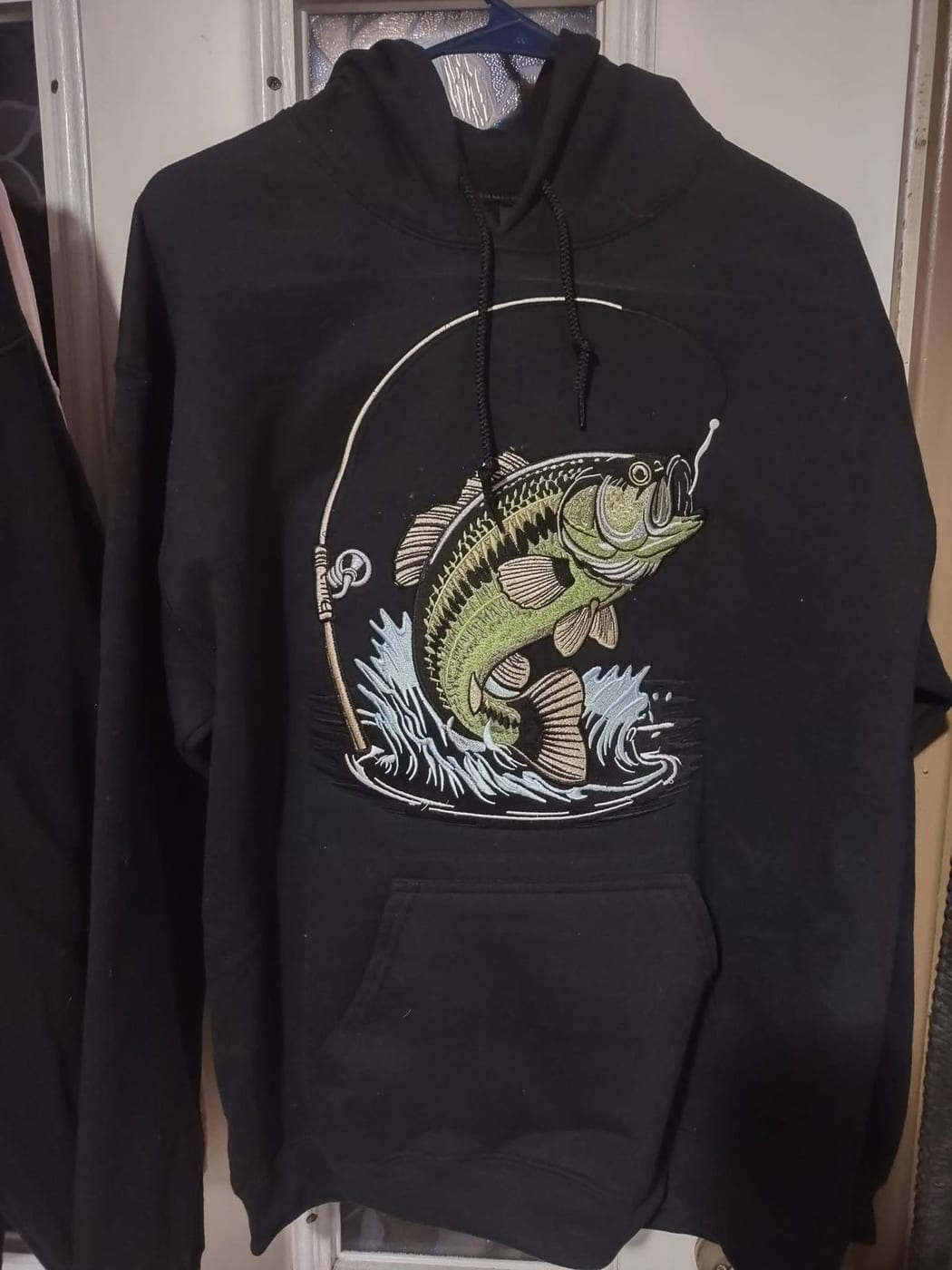 Black hoodie embroidered with a largemouth bass leaping out of the water at a fishing line